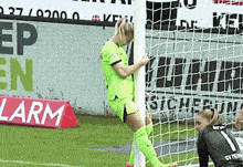 a female soccer player leans on a net in front of a sign that says alarm
