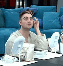 a man is sitting at a table with two mirrors and a bag of martin cosmetics .