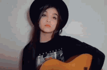 a young girl is holding a guitar and wearing a black hat .