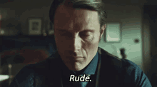 a man in a suit and tie is sitting in a dark room and saying `` rude '' .