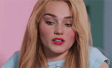 a woman with blonde hair and red lipstick is wearing a blue shirt and looking at the camera .