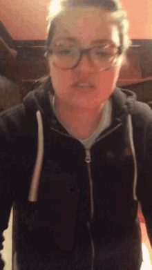 a woman wearing glasses and a black hoodie looks at the camera