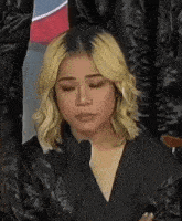 a woman with blonde hair is sitting in front of a microphone with her eyes closed