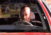 a bald man is driving a red car and looking out of the window
