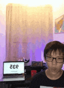 a boy wearing glasses is standing in front of a laptop with the number 332 on it
