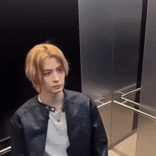 a man wearing a leather jacket and a white shirt is sitting in an elevator