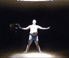 a shirtless man in underwear stands in a dark room