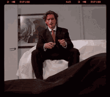 a man in a suit and tie is sitting on a bed with blood on his face and the number 465 on the bottom