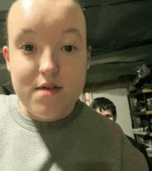 a young boy with a bald head is making a funny face while wearing a grey sweater .