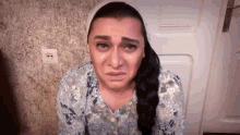 a woman is crying in front of a door while wearing a white head scarf .