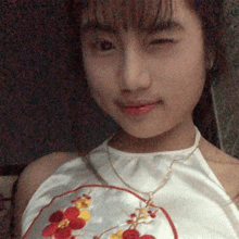 a close up of a woman wearing a white top with red and yellow flowers on it
