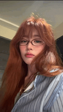a woman with long red hair and glasses is wearing a striped shirt