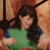 a woman in a green shirt is sitting at a table with a plate of food in front of her .