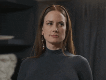 a woman wearing a turtleneck sweater and earrings looks at the camera