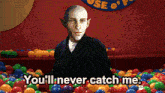 a bald man is standing in a ball pit and says you 'll never catch me