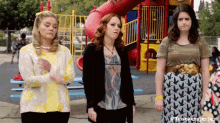 three women are standing in front of a playground with a slide .