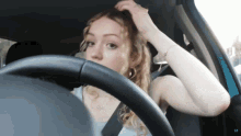a woman adjusts her hair while sitting in the driver 's seat