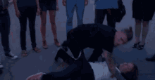 a group of people are standing around a man in a black shirt who is kneeling down .