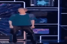 a man in a blue shirt is dancing on a stage in front of a wall .