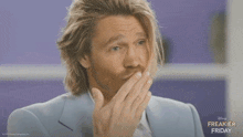 a man in a blue suit is covering his mouth with his hand while a freakier friday advertisement is behind him