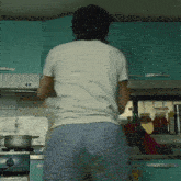 a man in a white shirt and blue shorts stands in a kitchen