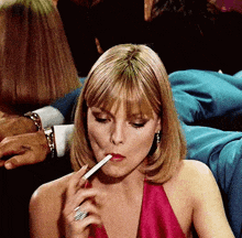 a woman in a red dress is smoking a cigarette in a crowded room .