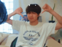 a young man is sitting on a bed with his arms outstretched and making a thumbs down sign .