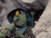 a green puppet wearing sunglasses and a hat is holding a stick