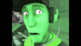a green cartoon character is wearing headphones and making a funny face .