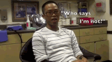 a man wearing glasses and a striped shirt is sitting in a chair and says " who says i 'm not "