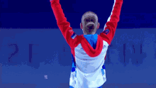 a woman in a red white and blue jacket holds her hands up in the air
