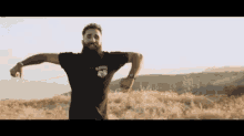 a man with a beard is standing on top of a hill with his arms outstretched .