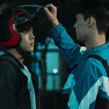 a man wearing a red and black helmet adjusts another man 's helmet
