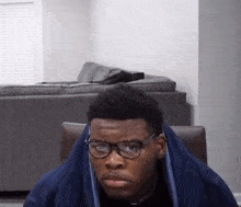 a young man wearing glasses and a blue blanket is sitting in a chair in a living room .
