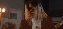 a man with long blonde hair wearing sunglasses is singing into a microphone .