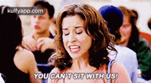 a woman is sitting in a crowd of people and saying you can 't sit with us .