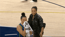 two women on a basketball court with one holding a shirt that says atg