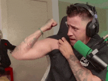 a man wearing headphones flexes his muscles in front of a microphone