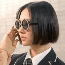 a woman wearing sunglasses and a suit has a hand covering her eyes