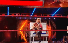 a woman is sitting in a chair in a wrestling ring holding a championship .