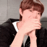 a young man with red hair is covering his mouth with his hands while wearing a black jacket .