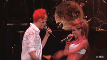 a man with red hair is singing into a microphone next to a woman with pink hair