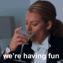 a woman in a tuxedo drinking a martini with the words we 're having fun behind her