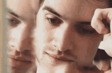 a man is looking at his reflection in a mirror while applying eye shadow .