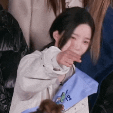a woman covering her mouth with her hand while holding a blue bag with the letter o on it .