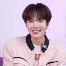 a young man in a pink sweater is making a funny face with his hands together .