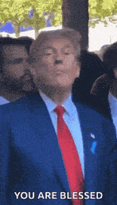 donald trump is wearing a blue suit and red tie and is standing in front of a crowd .
