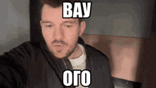 a man with a beard is wearing a black jacket and a white sweater and says bay oro