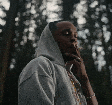 a man in a hoodie is smoking a cigarette in the woods