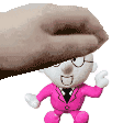 a hand is holding a stuffed toy with glasses and a pink suit .